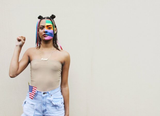 Persona con la bandera del orgullo pintada en la cara, alzando un puño por el movimiento Black Lives Matter