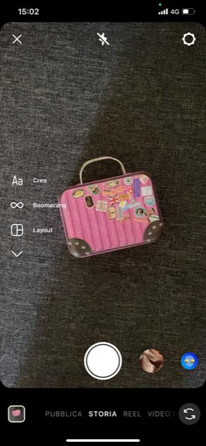 schermata della pagina dove scegli se utilizzare la fotocamera nelle Storie nell’app di Instagram o selezionare immagini già esistenti. si vede una valigia rosa su sfondo grigio